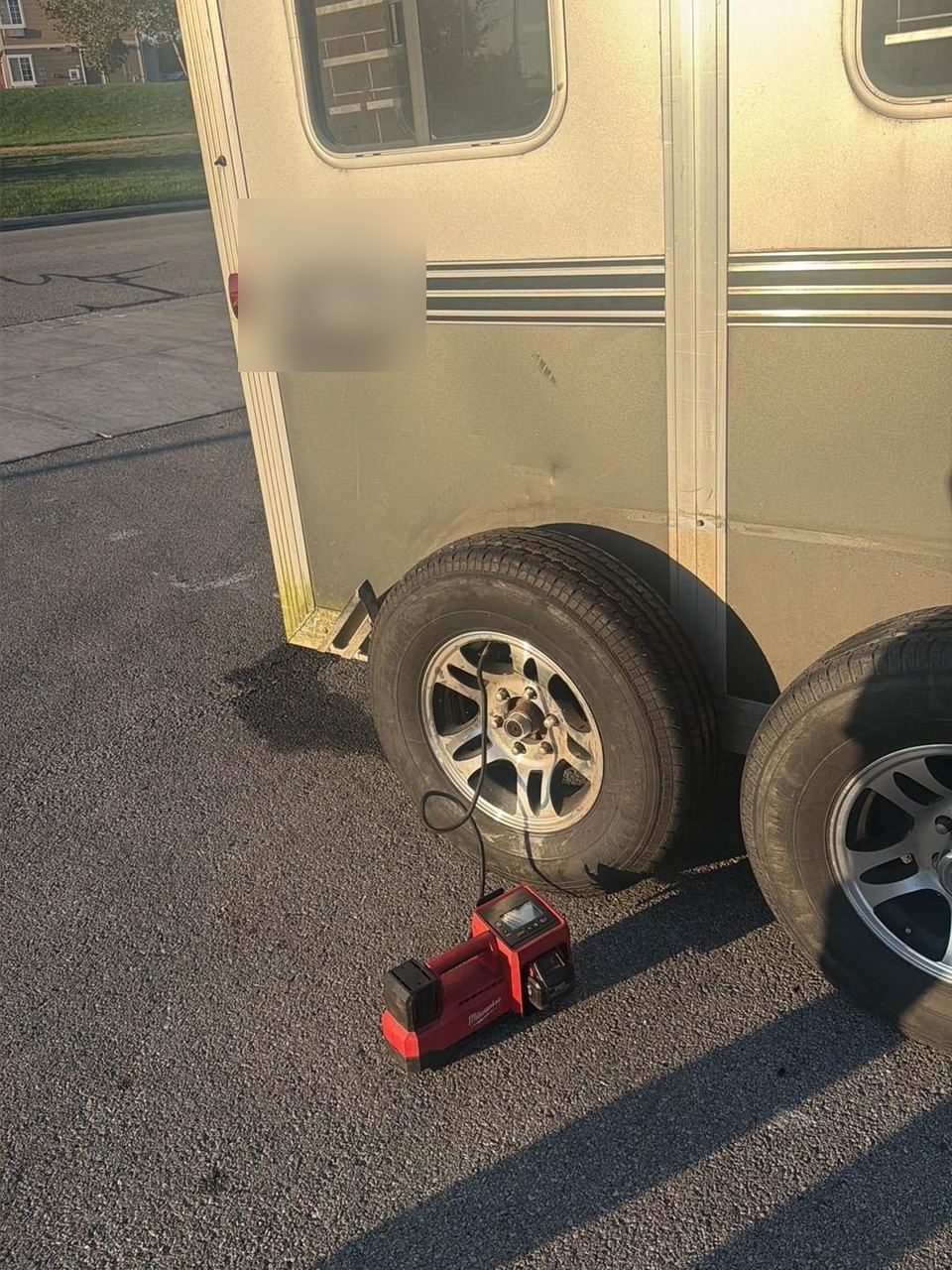 Red portable tire compressor on the pavement, its hose connected to a trailer tire