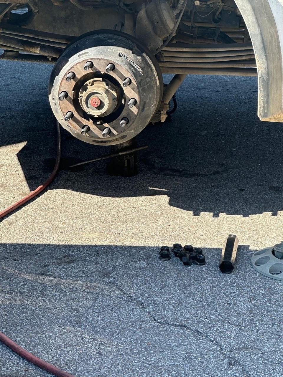 Wheel removed from a heavy-duty truck, showing the hub and brake drum, with the lug nuts set on the ground