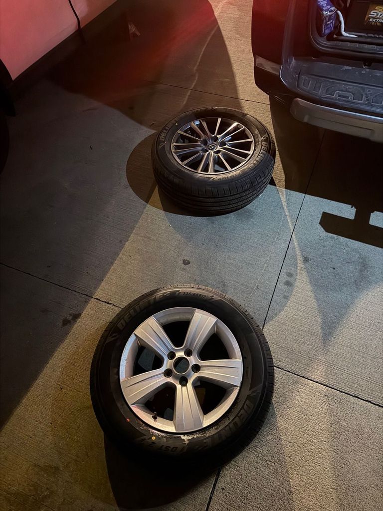 Two new tires on the ground at night, one on the original gray alloy wheel and one on a silver temporary wheel