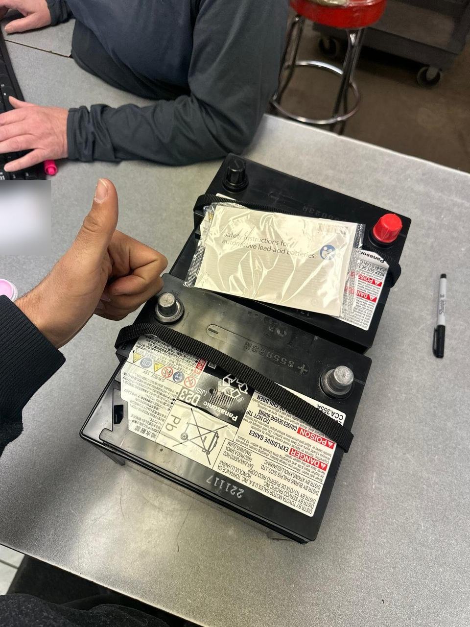 Two Panasonic car batteries on a parts counter, the front label showing CCA 355A, with a thumbs up beside them