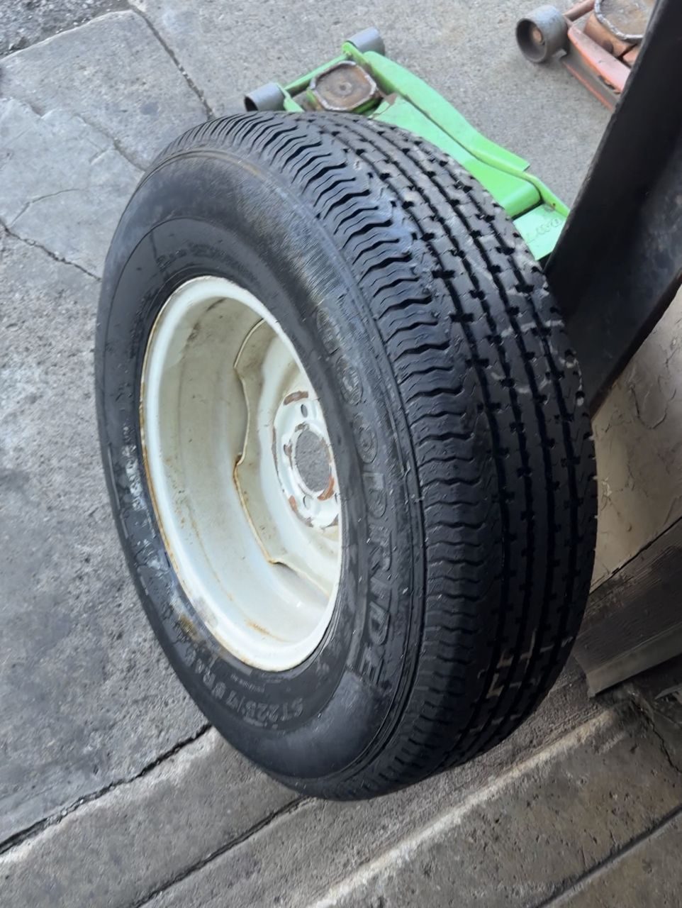 Used ST trailer tire mounted on a white steel trailer rim at the tire shop, ready to go back on the trailer