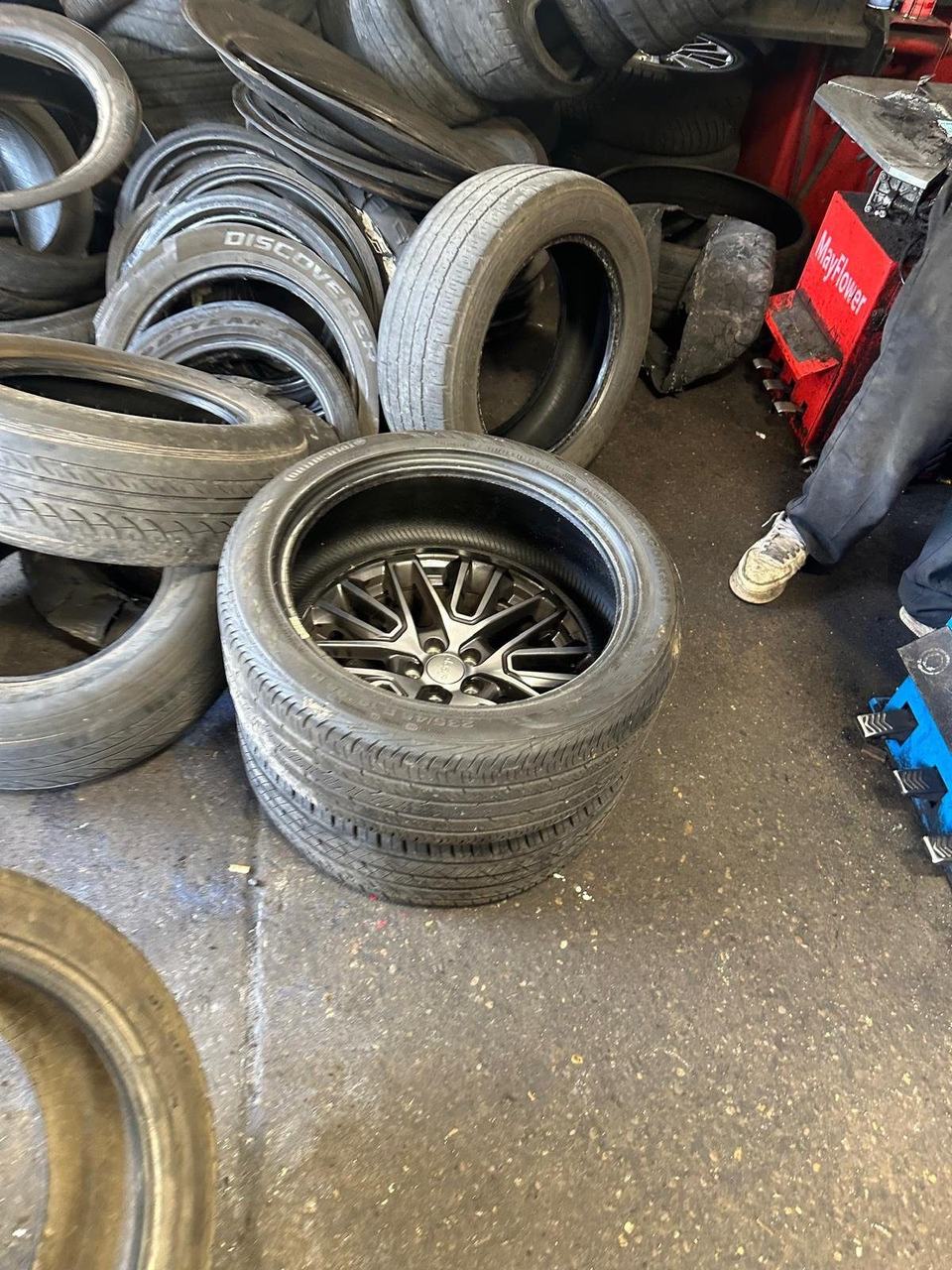 Used tires piled on a tire shop floor, with a stacked set on a wheel in front