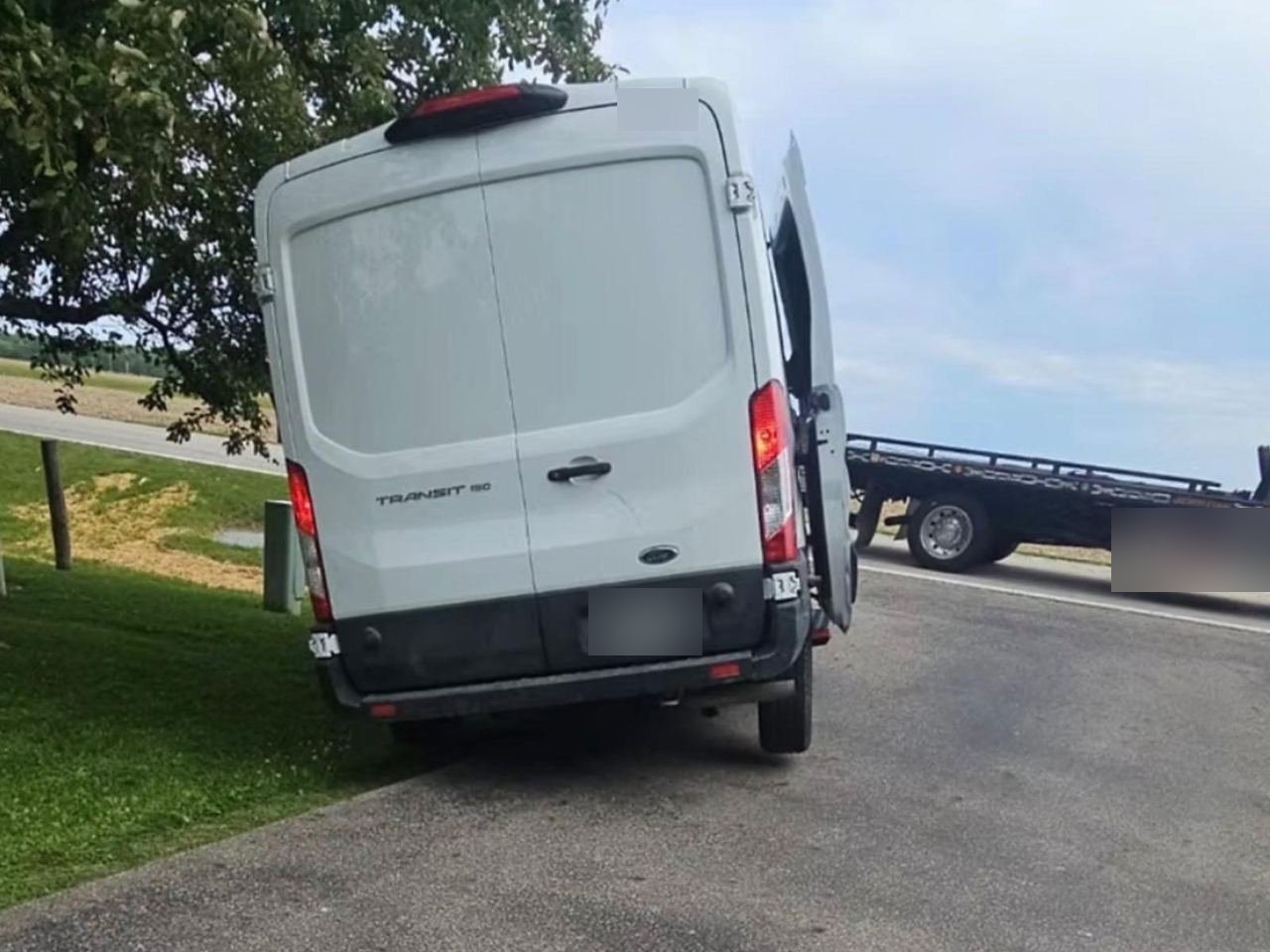 Disabled white Ford Transit van on the roadside with a flatbed tow truck pulling up behind it