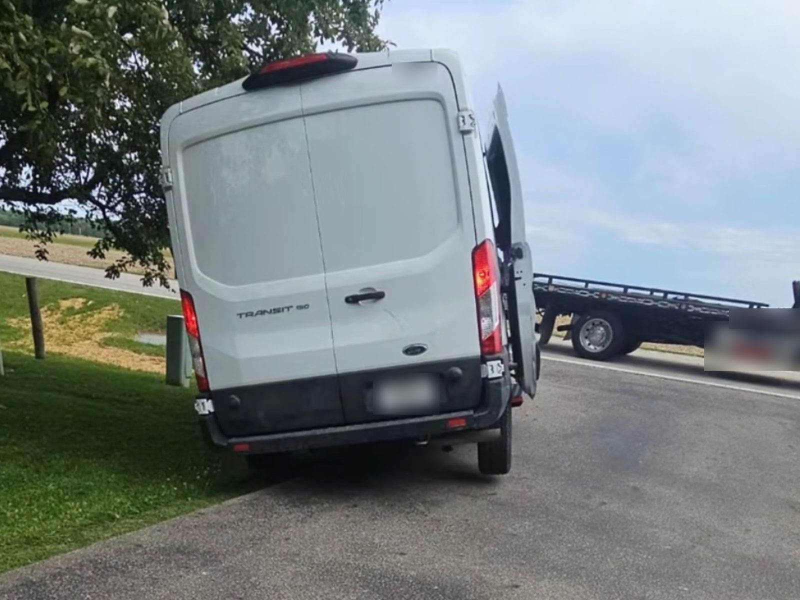 White cargo van with its wheels off the pavement on soft grass beside a road, waiting for a winch-out