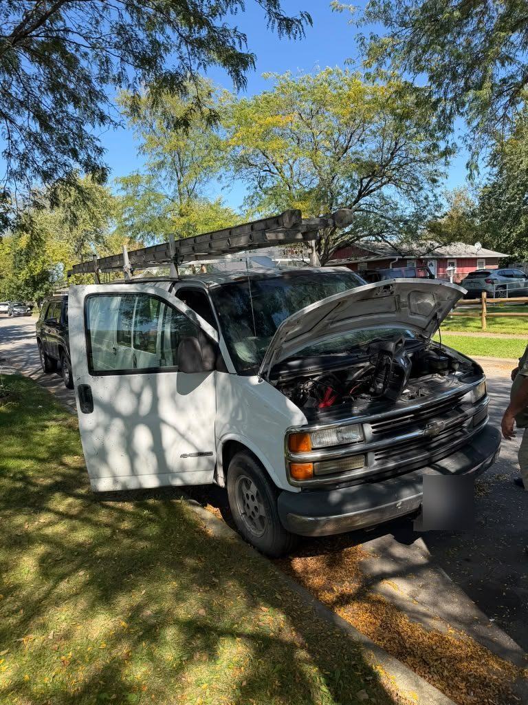 White work van with its hood open and a jump pack on the engine, parked on a residential street