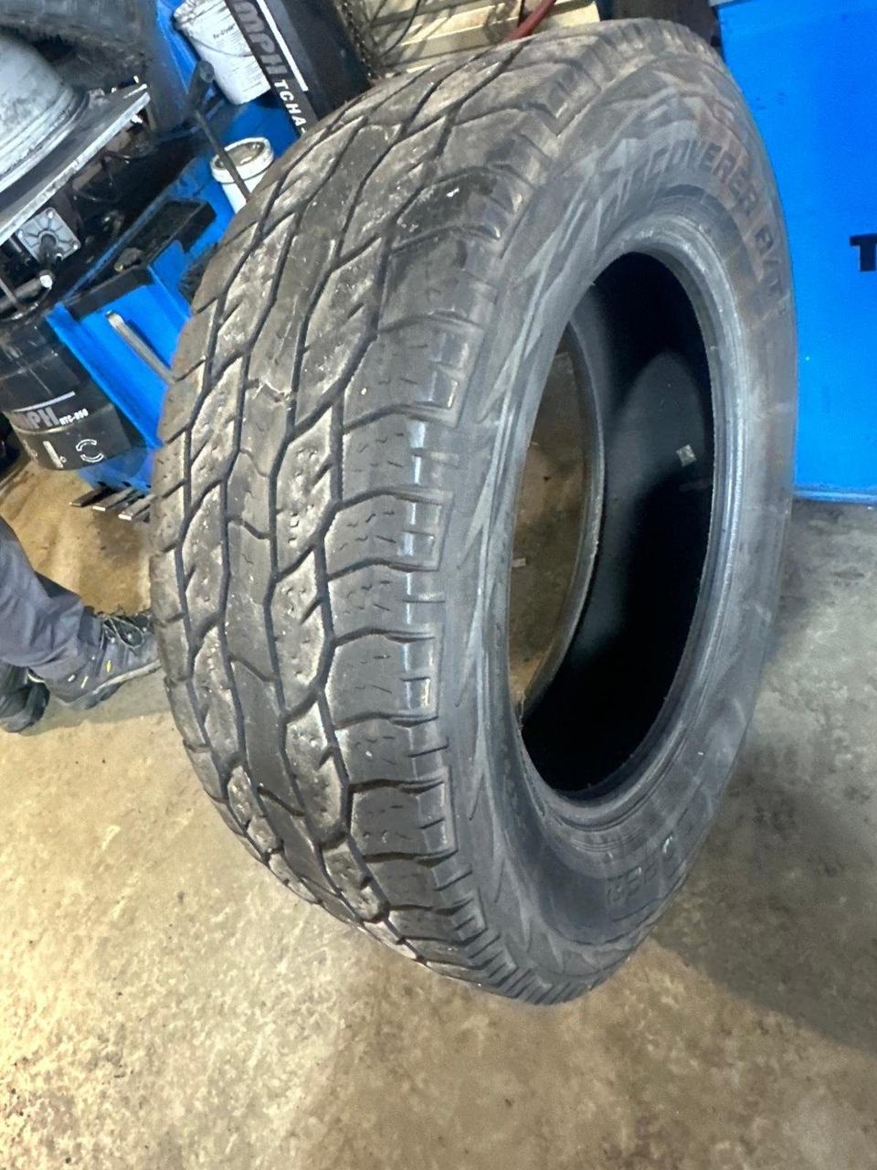 Worn all-terrain tire off the rim, standing next to a tire changing machine in a shop