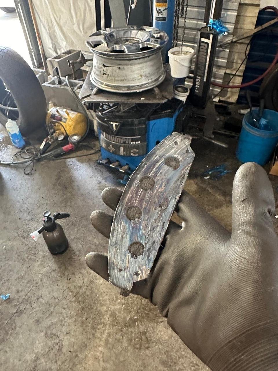 Worn brake pad held in a gloved hand, the friction material worn down to the metal backing plate